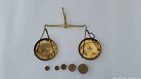 Front view of balance scale with two brass dishes and five brass weights arranged.