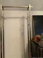 Front view of the tall, silver metal display rack standing against a wall with adjustable height mechanism visible.