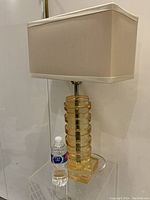 Full view of the large vintage lucite lamp with rectangular beige fabric shade and water bottle for size reference.