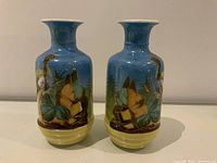 Front view of pair of small vintage vases with hand-painted bird and floral design on blue background