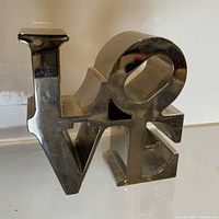 Front view of polished aluminum LOVE sculpture on white surface