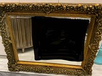 Front view of the large ornate gold-framed mirror showing the intricate floral and scrollwork details on the frame and clear reflective surface.
