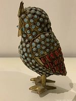 Side view of owl showing light blue and red stone beads and metal feet.