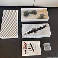 Full kit including outer checkered box, USB cable, SIM ejector tool, user manual, 32GB SD card in case, and the spy pen in molded plastic tray.