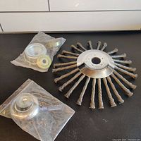 Photo showing one 10 inch steel wire brush trimmer head with twisted wire bristles and two metal mounting parts in plastic packaging.