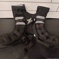 Front view of black padded weighted vest with adjustable straps and reflective stripes, showing buckle closure and padding detail.