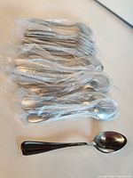 20 stainless steel demitasse spoons stacked and individually wrapped in plastic, laid on a flat surface.