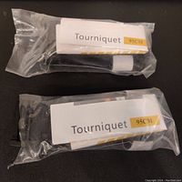 Two black emergency trauma tourniquets packaged separately in clear plastic with white and yellow labels reading 'Tourniquet 95CM'