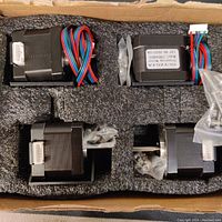 Four Nema 17 stepper motors in foam packaging inside a box showing the motors laid out with wiring and connector cables attached accompanied by screws.