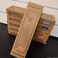 Photo of six unopened biodegradable cardboard boxes for cutlery sets each with cutlery silhouette and a visible color strip showing the set color.