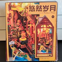 Front of the packaging showing the miniature town model with canal and warm lights inside a book-shaped structure.