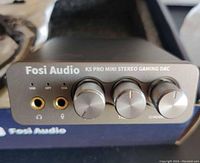 Front view of black Fosi Audio device with headphone and microphone jacks plus three control knobs labeled volume, treble, and mode.