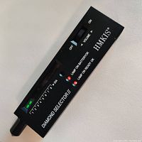 Front view of black handheld electronic diamond tester pen with digital display, lights and volume switch labeled Diamond Selector II by HMKIS.