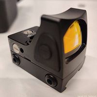 Close view of the black reflex sight showing the tinted lens and black metal housing with adjustment controls.