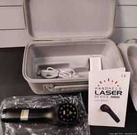 Photo showing the handheld laser device, carrying case, USB charging cable, and user manual arranged for display.