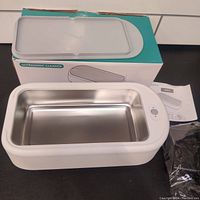 Top view of the ultrasonic jewelry cleaner with its box, showing the stainless steel interior tank and a control button on the device body.