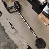 Full length view of the metal detector showing the shaft, armrest, and circular search coil on a table.