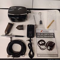 Complete set including compressor, airbrush, hose, brushes, needle, adapter, and manual laid out on a flat surface