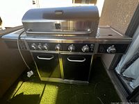 Front view of the large black and gray gas barbecue grill with closed lid, multiple burners, and double-door storage below.