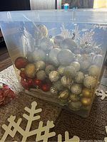 Plastic container filled with gold, silver, and red Christmas ornaments of various shapes and textures.