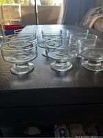 Four transparent glass sundae ice cream bowls with round base and pedestal, placed on wooden surface