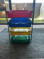 Front view of the paper tray organizer showing the stacked colorful trays with red on top and green on bottom, set on carpet with outdoor background.