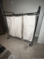 Full view of three-section laundry hamper sorter with metal frame on wheels and white fabric bags.