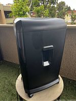 Front view of the tall black paper and CD shredder showing its sleek design, handle, and wheels.