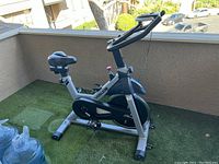 Full side view of the YOSUDA indoor cycling bike showing silver frame, black cushioned seat, and iPad mount on handlebars.