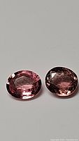Two oval cut multicolored (pink, purple, orange) tourmaline gemstones on white surface, showing clarity and color variation