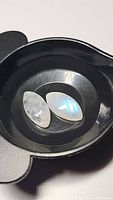 Close-up of two natural rainbow moonstone cabochons, marquise and teardrop shaped, on black surface showing blue and rainbow flash.