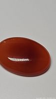 Close-up photo showing a deep orange oval carnelian cabochon with smooth polished surface and glossy finish.