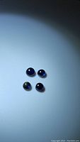 Four round blue sapphire cabochons arranged on a white surface under lighting to show color and transparency.