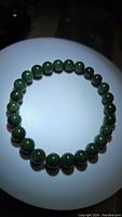 Top-down view of green polished jade bead bracelet under direct light showing bead shine and round shape.