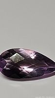 Close-up view of the natural amethyst gemstone showing its pear shape and checkerboard cut with pink and purple color hues.