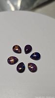 Six purple copper turquoise cabochon gemstones with pear and oval shapes, displaying copper matrix inclusions.