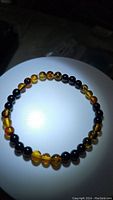 Bracelet composed of alternating natural Baltic amber and jet black onyx beads arranged on a stretchy band, shown on a white circular platform against a dark background.
