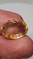 Close-up image showing faceted oval natural golden citrine gemstone held between fingers, highlighting clarity and color.