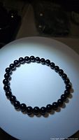 Top-down view of natural jet black onyx bead stretchy bracelet displayed on a circular white platform, beads glossy and round.