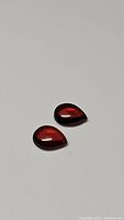 Two pear-shaped cherry red garnet cabochons on white background.