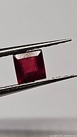 Close-up photo of square cut blood red ruby held between tweezers showing depth of color and cut facets