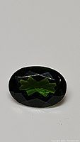 Close-up photo of oval cut natural chrome diopside displaying deep electric green color and faceted surface.