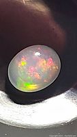 Close-up image showing oval cabochon cut Ethiopian opal with bright green and red color flashes.
