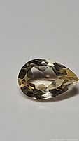 Close-up photo of a natural golden citrine gemstone, pear cut, faceted, measuring 12x8mm