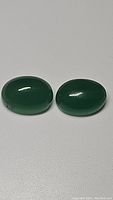 Two oval cabochon green aventurine gemstones on a white background.