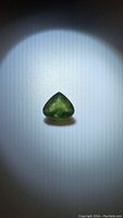 Close-up photo of the green sapphire gemstone under white light showing the pear cut shape and color.