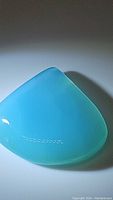 Close-up photo of large pear-shaped icy blue chalcedony cabochon gemstone with smooth, polished surface and glowing effect under light.