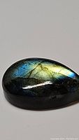Close-up image of pear-shaped natural labradorite polished cabochon showing golden and blue flash on dark body.