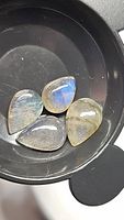 Four pear cabochon natural labradorite stones in a black container showing their coloration and flash.