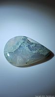 Top view of the pear-shaped natural moss agate cabochon showing translucent white base with green mossy patterns.
